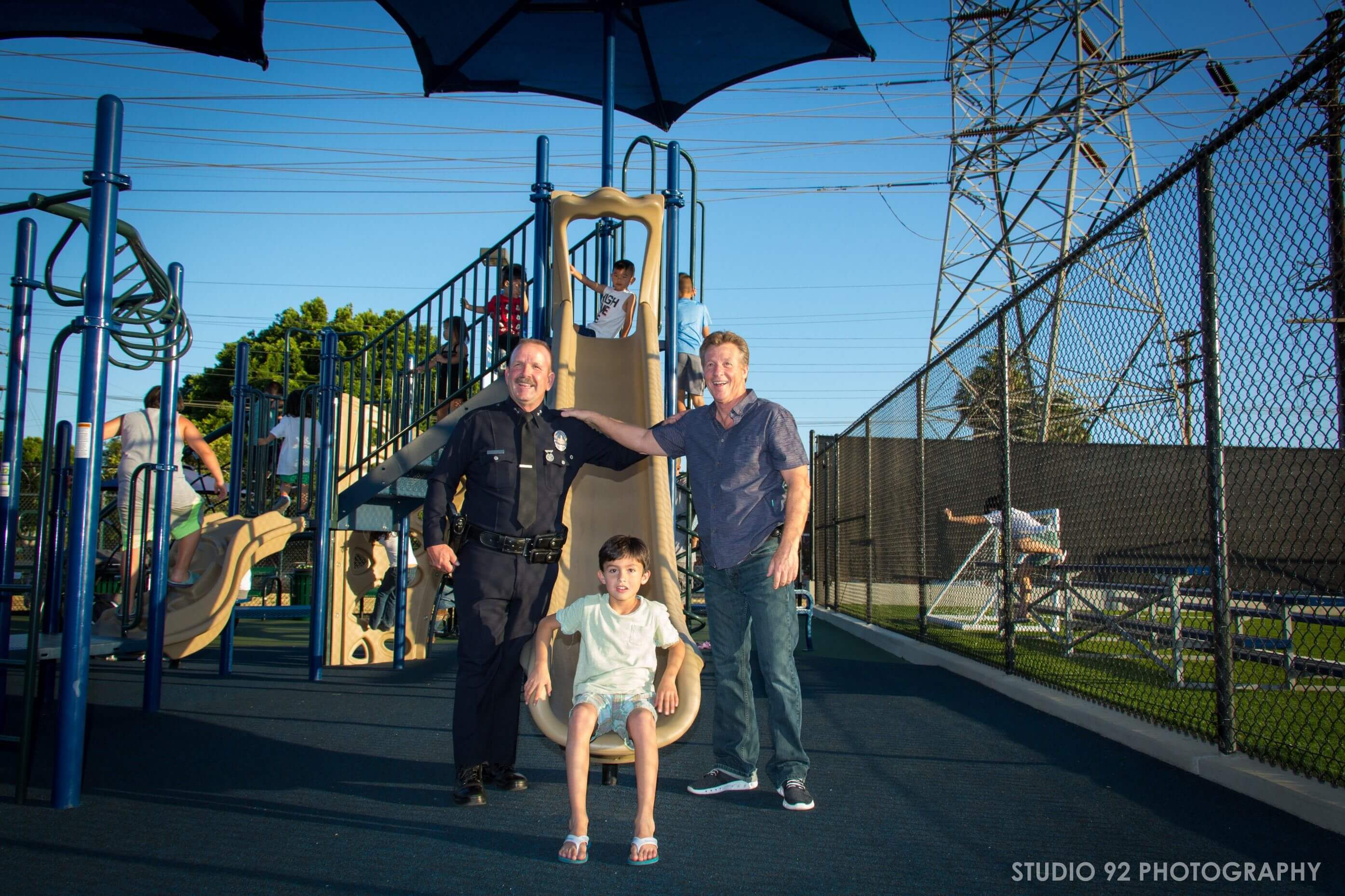 A police officer stands with an adult and a child on a new playground.